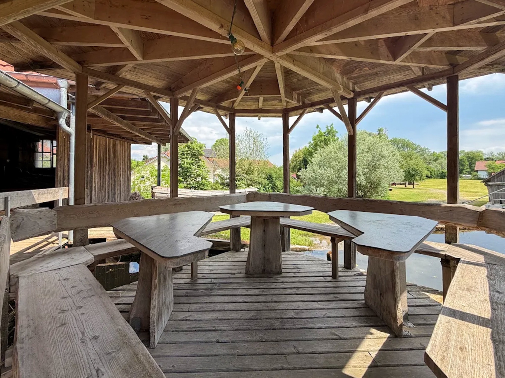 Der überdachte Pavillon der Oberen Mühle über dem Wasser, mit umlaufender Bank und Tisch in der Mitte