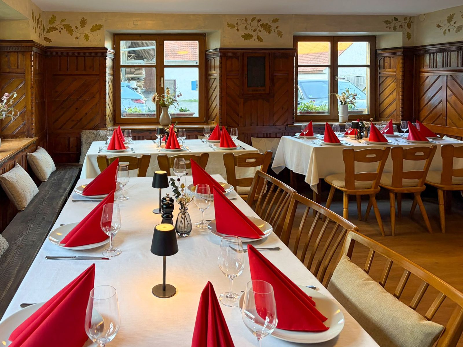 Der renovierte Raum im Haus, eingedeckt für eine Feier: lange Tafel mit weißem Tischtuch, roten Servietten und Tischlampen vor Holztäfelung